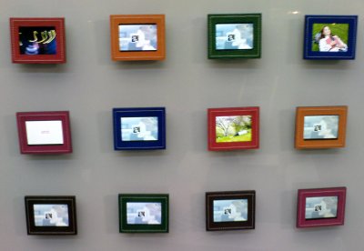 12 digital picture frames hanging on a wall, each with a different colour frame