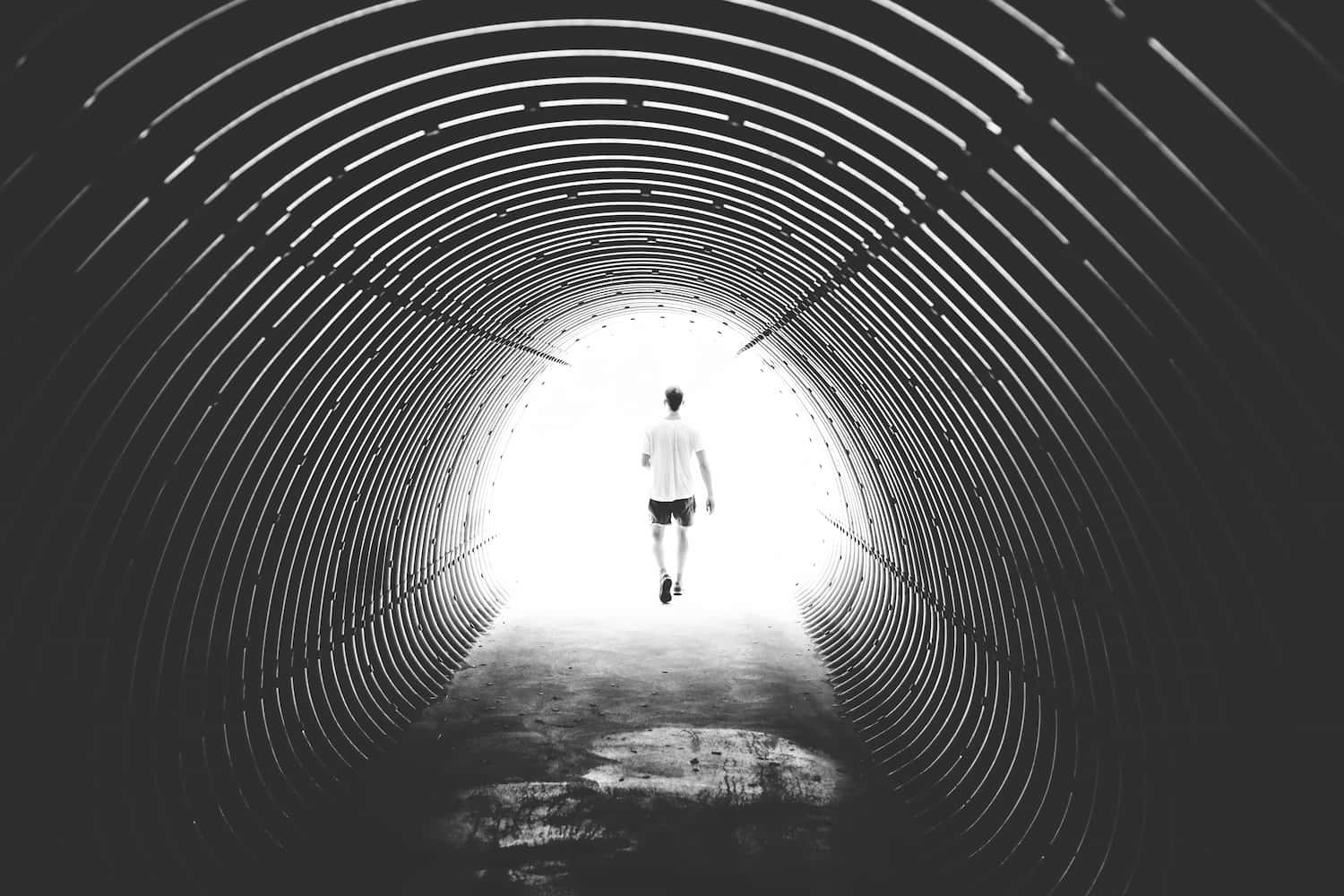 A man walks out of a dark tunnel towards a bright light