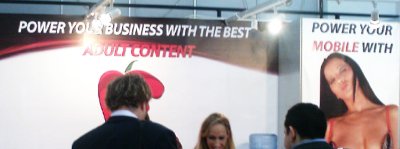 A poster at a stand reads: "Power your business with the best adult content". Beside it, another poster is titled "Power your mobile with" and below is a photo of a woman in lingerie.